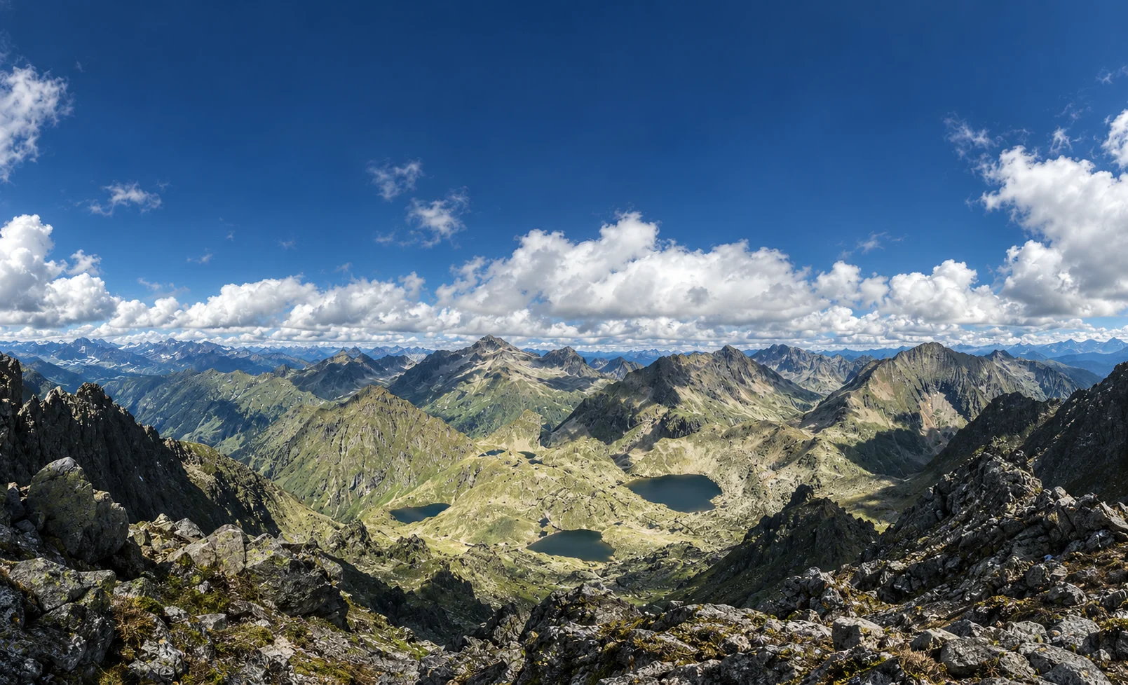 A wide mountain landscape with distant ridges, lakes and a quiet sky